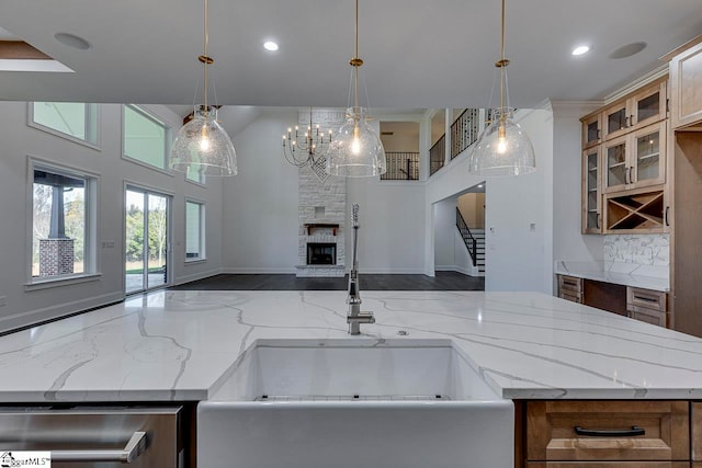 kitchen featuring stainless steel dishwasher, light stone counters, decorative light fixtures, a notable chandelier, and a stone fireplace