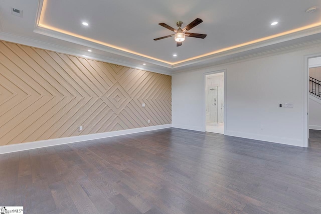 empty room featuring ornamental molding, a raised ceiling, ceiling fan, dark wood-type flooring, and wood walls