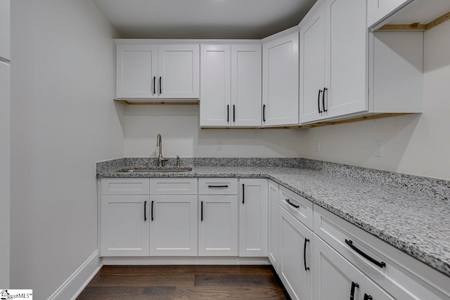 kitchen featuring dark hardwood / wood-style flooring, light stone counters, white cabinetry, and sink