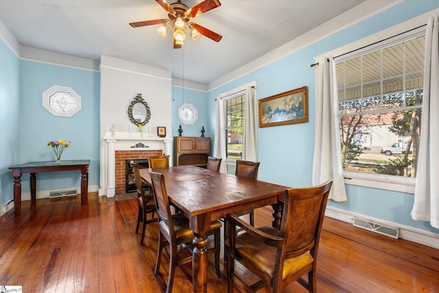 dining area with ceiling fan, dark hardwood / wood-style flooring, and a brick fireplace