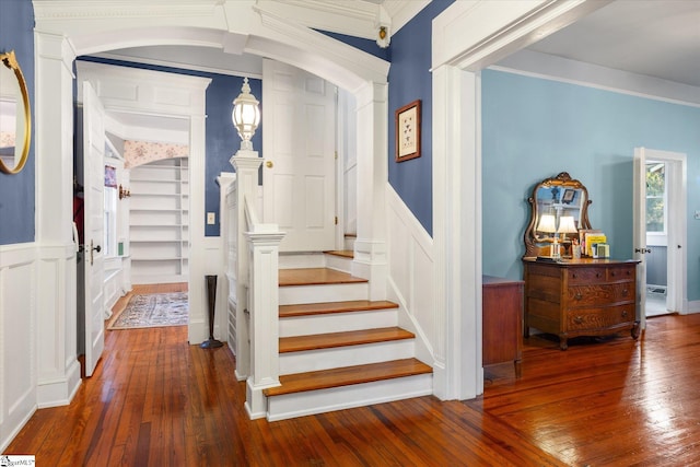 stairway with ornate columns, wood-type flooring, and ornamental molding