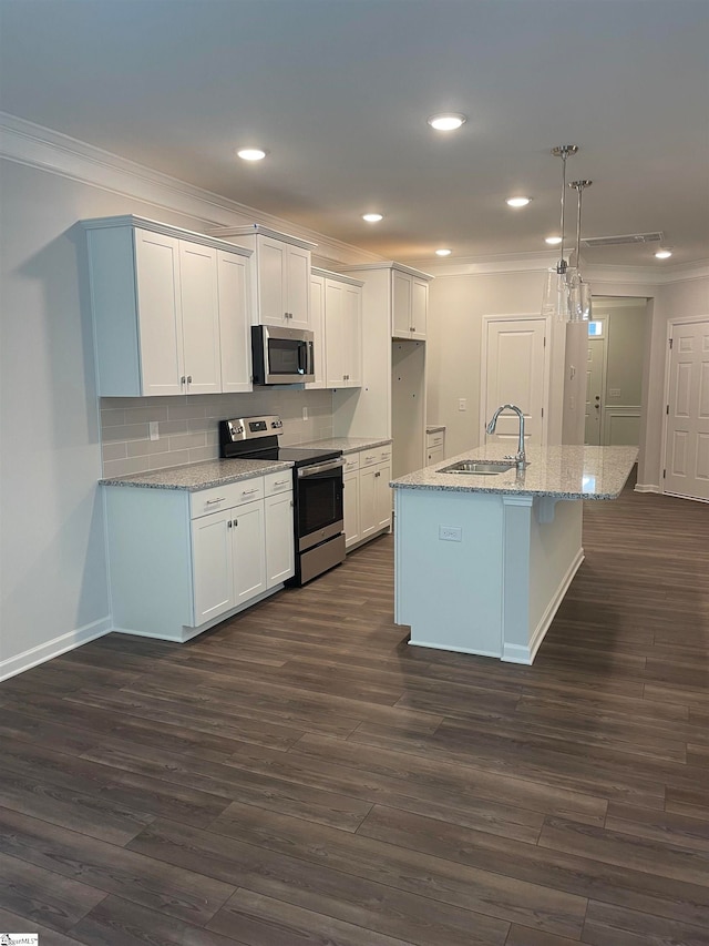 kitchen with white cabinets, appliances with stainless steel finishes, decorative light fixtures, and a kitchen island with sink