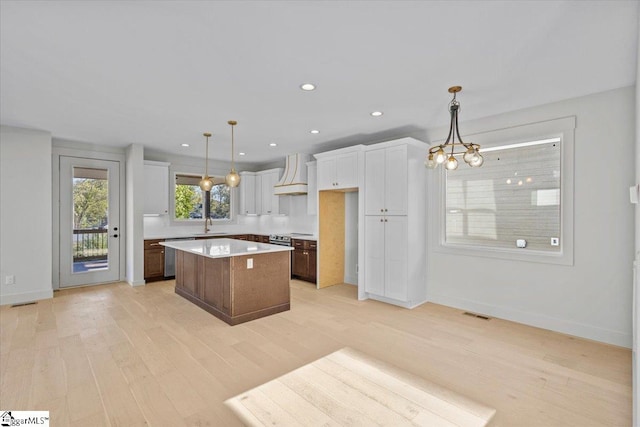 kitchen featuring white cabinets, custom range hood, a center island, and decorative light fixtures