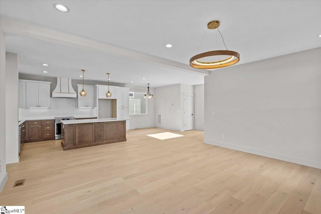 kitchen featuring a center island, hanging light fixtures, stainless steel range oven, custom range hood, and light wood-type flooring