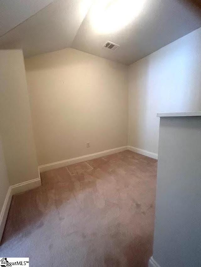 carpeted spare room featuring baseboards, visible vents, and vaulted ceiling