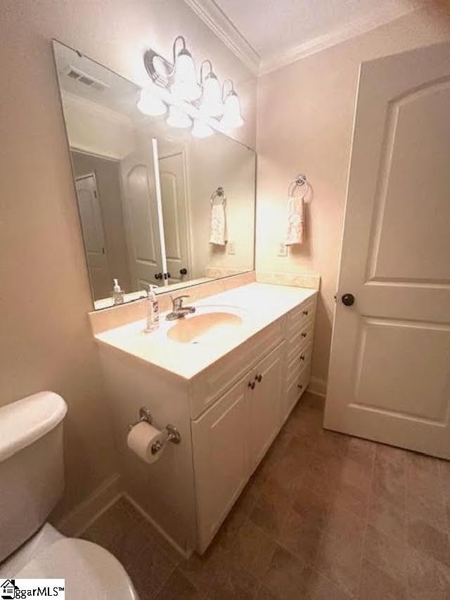 half bathroom featuring visible vents, ornamental molding, vanity, and toilet