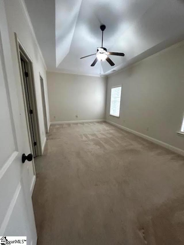 empty room featuring baseboards, a tray ceiling, a ceiling fan, and light colored carpet