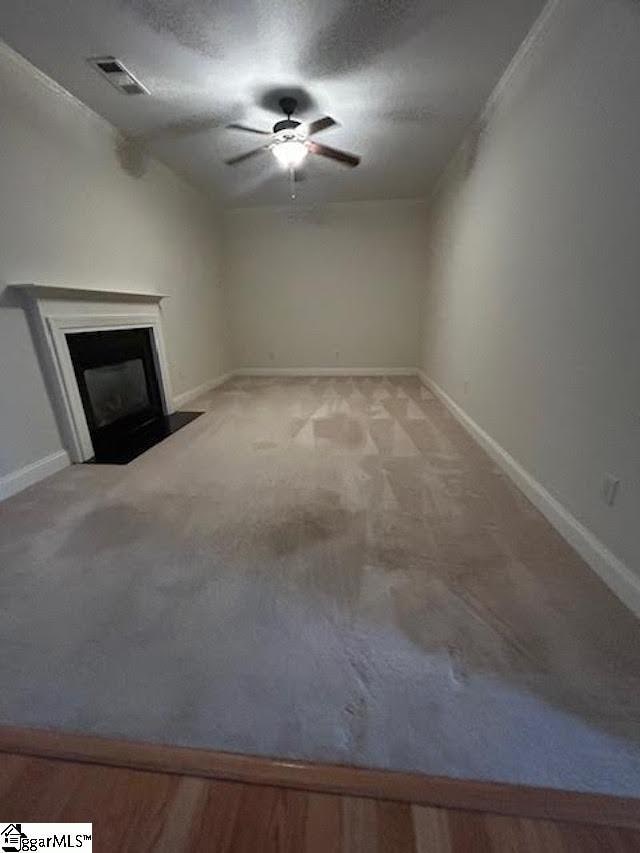 unfurnished living room with ceiling fan, a fireplace with flush hearth, visible vents, and baseboards