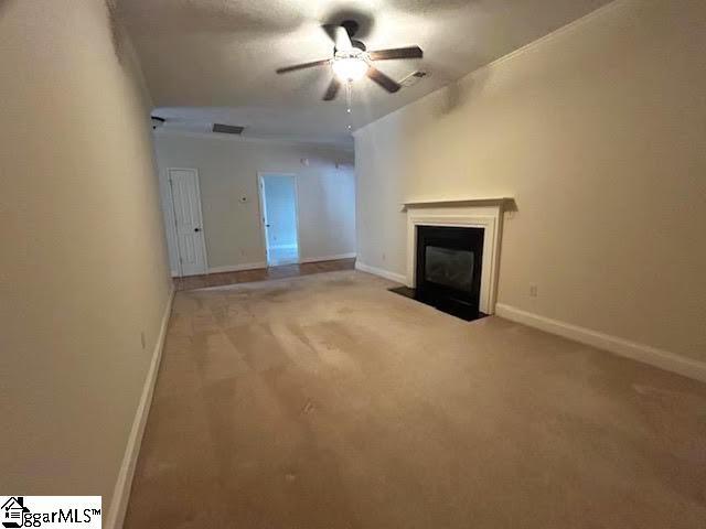 unfurnished living room with carpet, visible vents, a fireplace with flush hearth, a ceiling fan, and baseboards