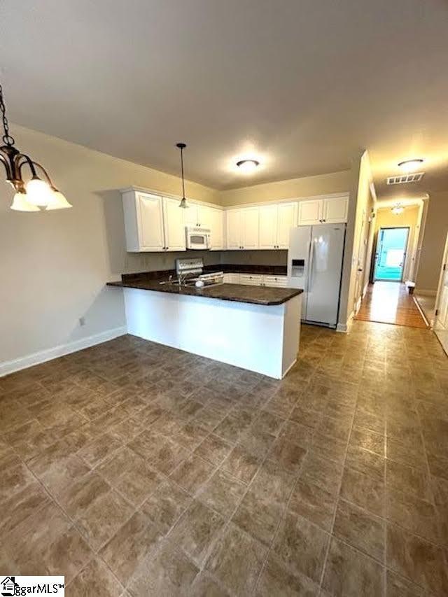 kitchen with hanging light fixtures, white appliances, dark countertops, and white cabinetry