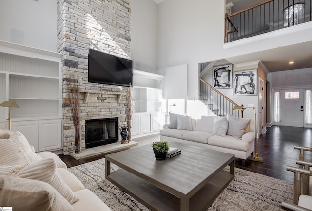 living room featuring a high ceiling, dark hardwood / wood-style floors, a stone fireplace, and built in shelves