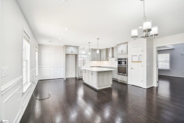 kitchen featuring a healthy amount of sunlight, a kitchen island, pendant lighting, and wall chimney range hood