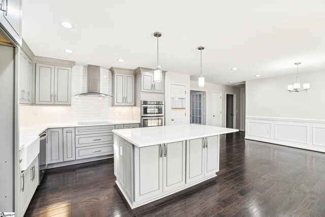 kitchen featuring a center island, decorative light fixtures, gray cabinetry, and wall chimney range hood