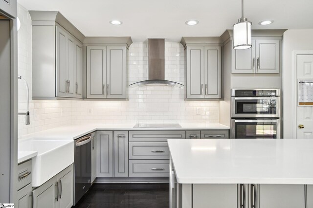 kitchen featuring gray cabinetry, wall chimney range hood, backsplash, pendant lighting, and appliances with stainless steel finishes