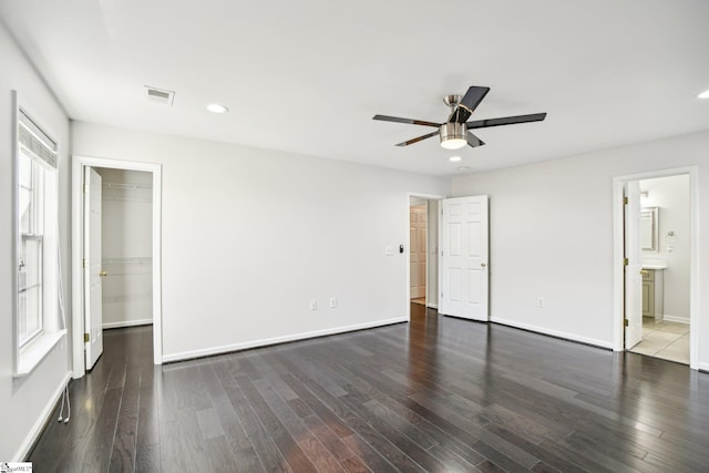 unfurnished bedroom featuring a walk in closet, ensuite bathroom, ceiling fan, dark wood-type flooring, and a closet