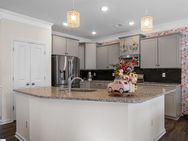 kitchen with stainless steel appliances, a kitchen island with sink, sink, pendant lighting, and a chandelier