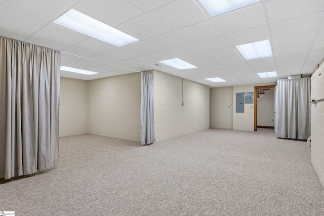 basement with a paneled ceiling, light carpet, and electric panel