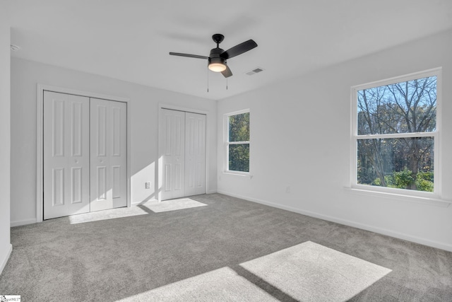 unfurnished bedroom featuring multiple windows, ceiling fan, light carpet, and multiple closets