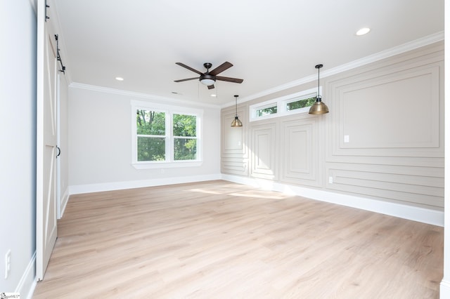 empty room with ceiling fan, a barn door, ornamental molding, and light hardwood / wood-style flooring