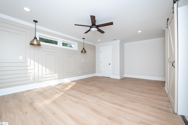 unfurnished living room with light wood-type flooring, a barn door, ornamental molding, and ceiling fan