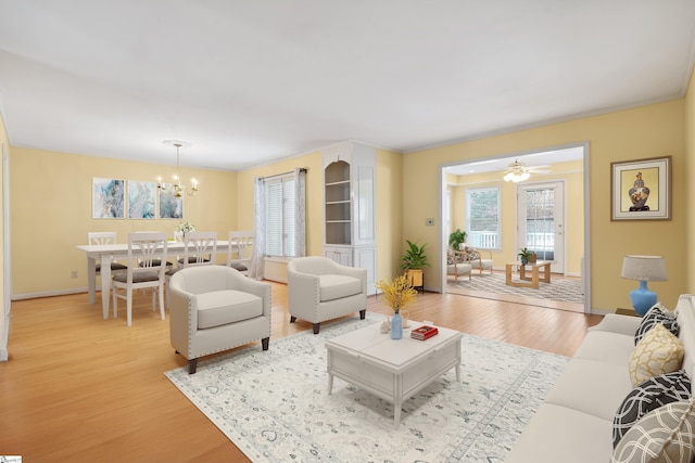 living room featuring baseboards, ceiling fan with notable chandelier, and light wood finished floors