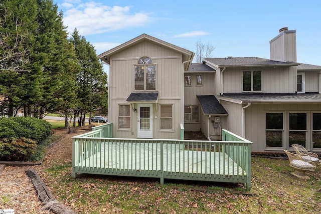 back of property with a shingled roof, a deck, and a chimney