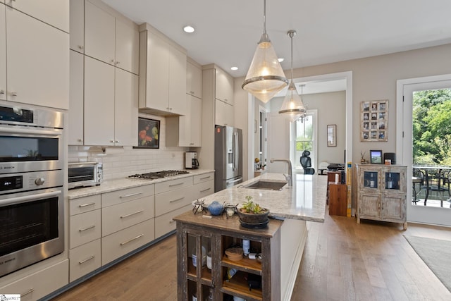 kitchen with light stone countertops, sink, stainless steel appliances, decorative light fixtures, and hardwood / wood-style flooring