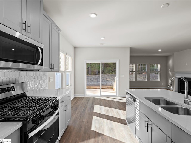 kitchen with sink, light hardwood / wood-style flooring, backsplash, gray cabinets, and appliances with stainless steel finishes