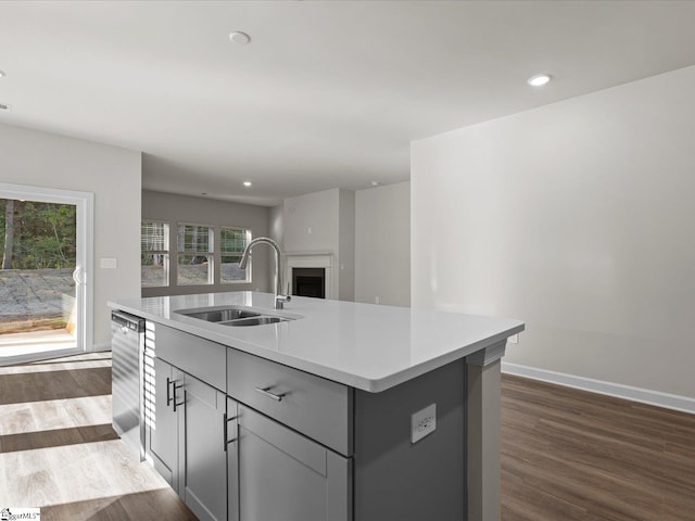 kitchen with gray cabinetry, dishwasher, sink, dark wood-type flooring, and a center island with sink