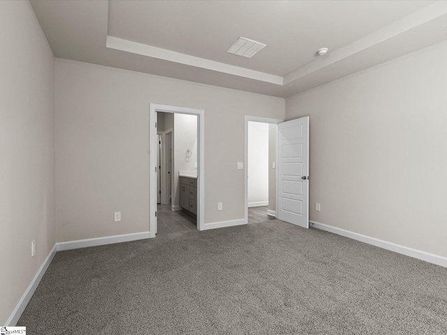 unfurnished bedroom with a raised ceiling, ensuite bathroom, and carpet