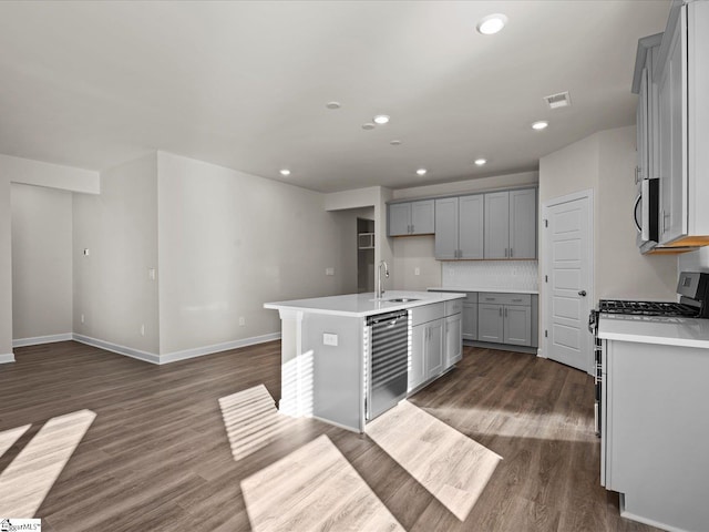 kitchen featuring decorative backsplash, dishwashing machine, dark wood-type flooring, sink, and a center island with sink