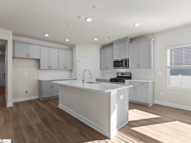 kitchen with stainless steel appliances, gray cabinets, a center island with sink, and sink