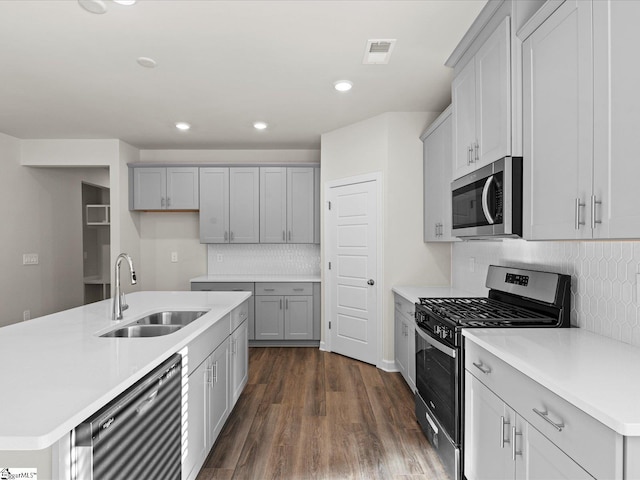 kitchen featuring gray cabinetry, stainless steel appliances, dark wood-type flooring, sink, and a center island with sink