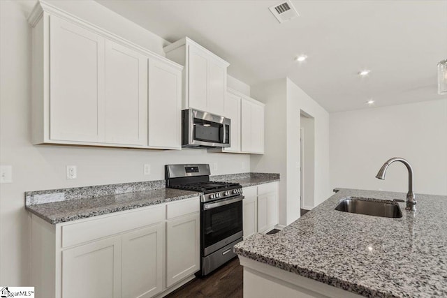 kitchen with appliances with stainless steel finishes, light stone counters, dark wood-type flooring, sink, and white cabinetry