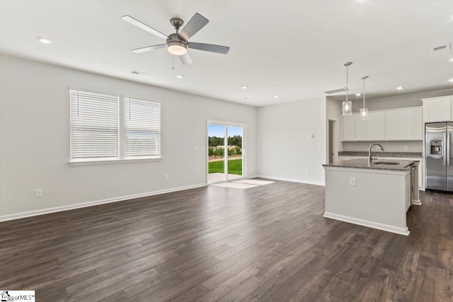 kitchen featuring stainless steel fridge, dark hardwood / wood-style flooring, dark stone counters, white cabinetry, and an island with sink