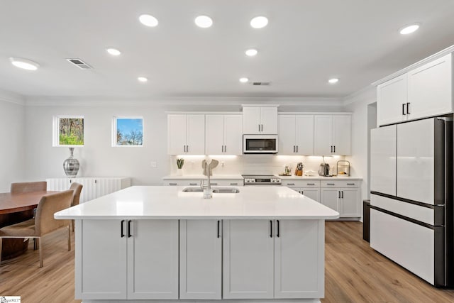 kitchen featuring white appliances, a kitchen island with sink, crown molding, sink, and white cabinetry