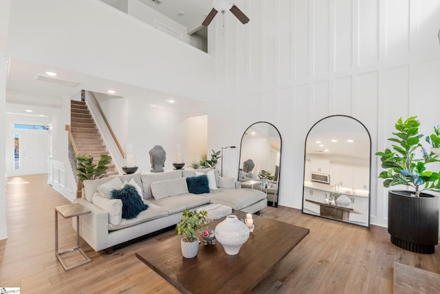 living room featuring ceiling fan, a towering ceiling, and light wood-type flooring