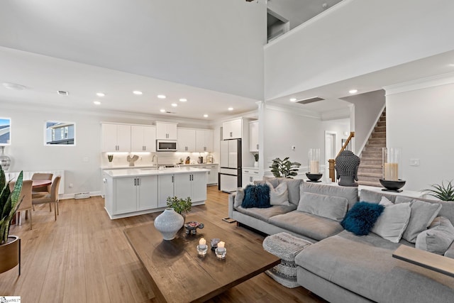 living room featuring sink, light wood-type flooring, ornamental molding, and a high ceiling