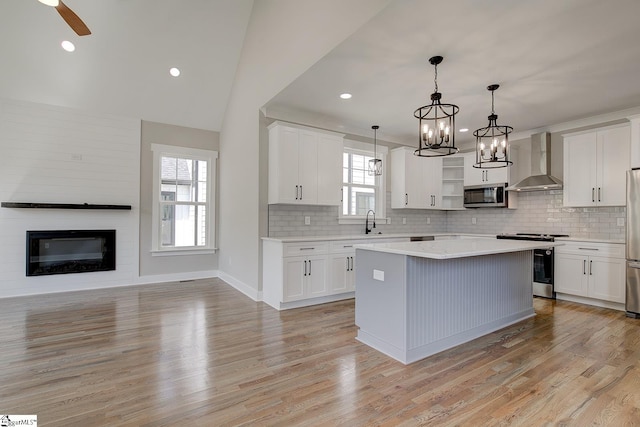 kitchen with appliances with stainless steel finishes, wall chimney exhaust hood, pendant lighting, white cabinets, and a center island