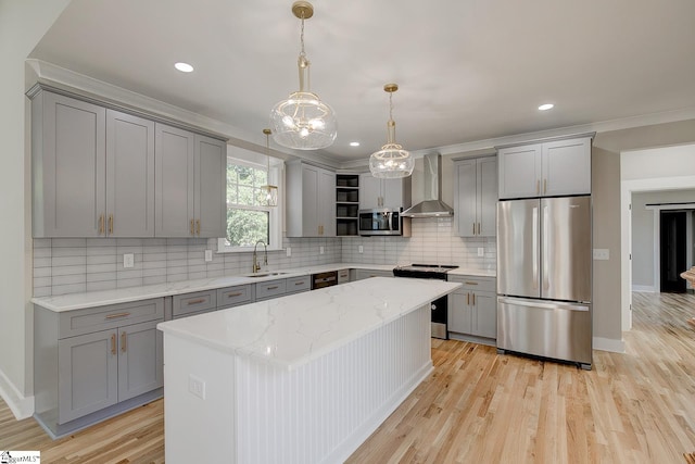 kitchen featuring a center island, sink, wall chimney exhaust hood, appliances with stainless steel finishes, and decorative light fixtures