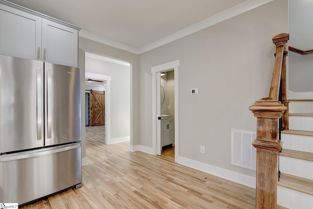 kitchen featuring stainless steel fridge, a barn door, light hardwood / wood-style floors, and crown molding