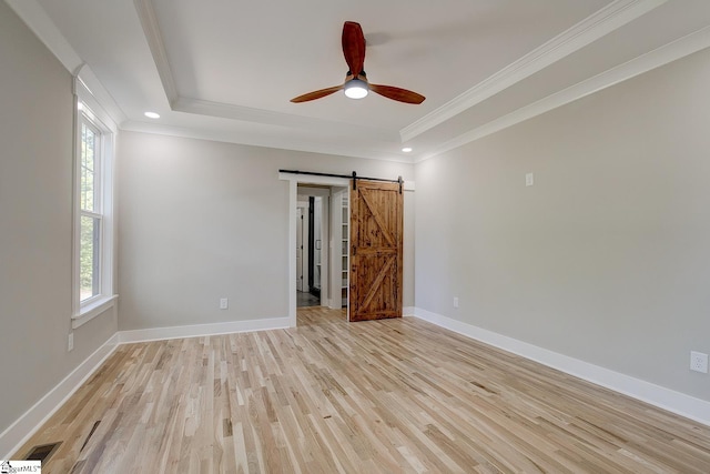 empty room featuring a barn door, light hardwood / wood-style floors, a raised ceiling, and ornamental molding