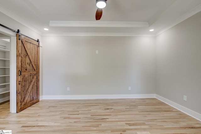 spare room with a barn door, crown molding, light hardwood / wood-style flooring, and ceiling fan