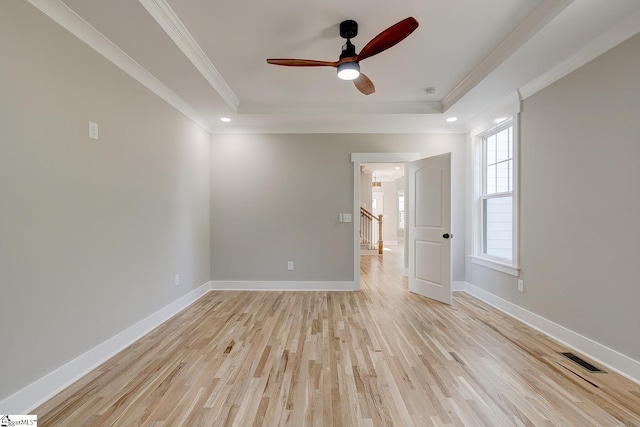 empty room with light wood-type flooring, a tray ceiling, ceiling fan, and ornamental molding