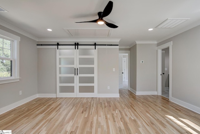 empty room with a barn door, light hardwood / wood-style flooring, ceiling fan, and ornamental molding