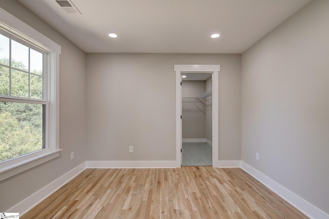 unfurnished bedroom featuring light hardwood / wood-style floors, a walk in closet, a closet, and multiple windows