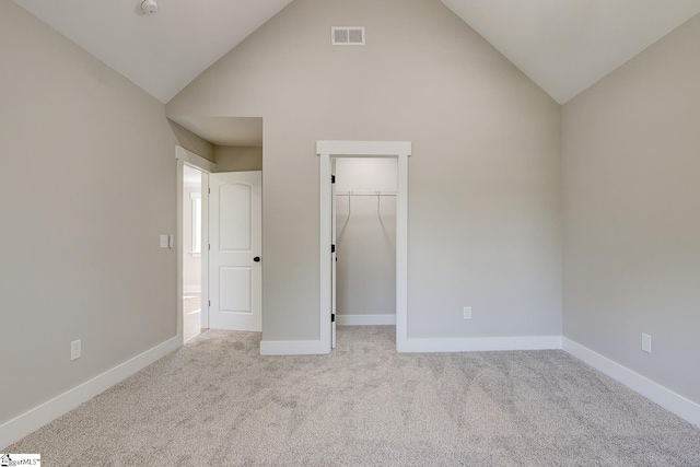 unfurnished bedroom with a spacious closet, a closet, light colored carpet, and lofted ceiling