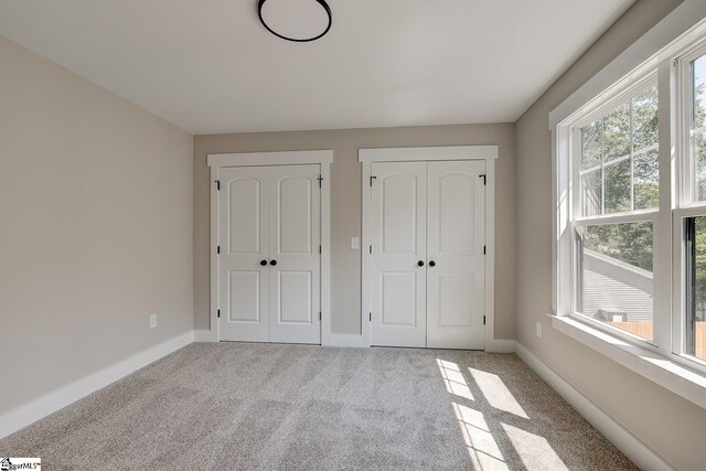 unfurnished bedroom with light carpet and two closets