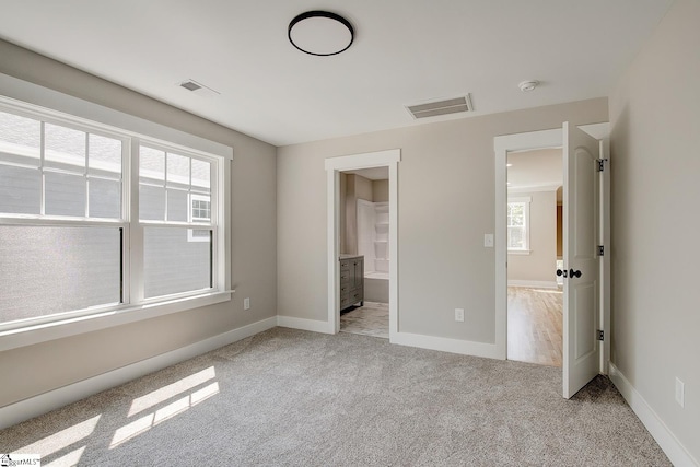 unfurnished bedroom featuring ensuite bathroom and light carpet