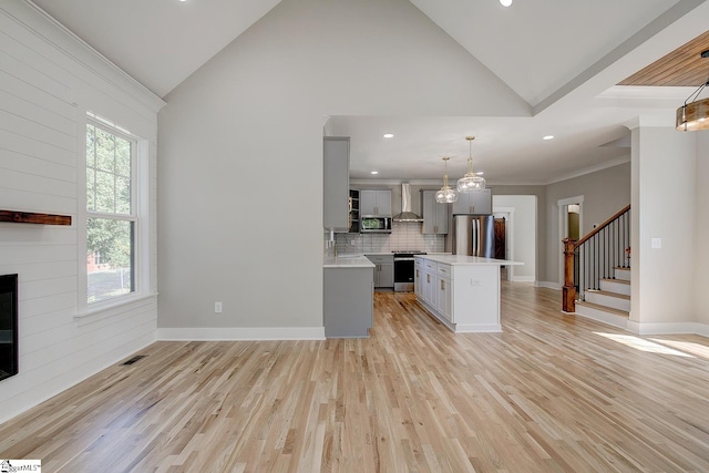 kitchen with wall chimney exhaust hood, stainless steel appliances, pendant lighting, a center island, and light hardwood / wood-style floors